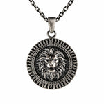 A silver-toned round pendant necklace featuring a detailed lion head design in the center, suspended from a matching chain against a plain white background.