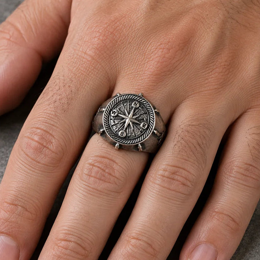 A silver-toned Viking-style ring with an embossed compass design, shown worn on a person's ring finger against a textured gray background.
