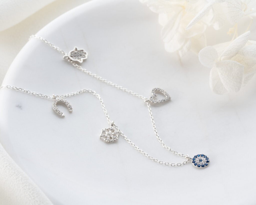 silver multi-charm anklet displayed on white surface