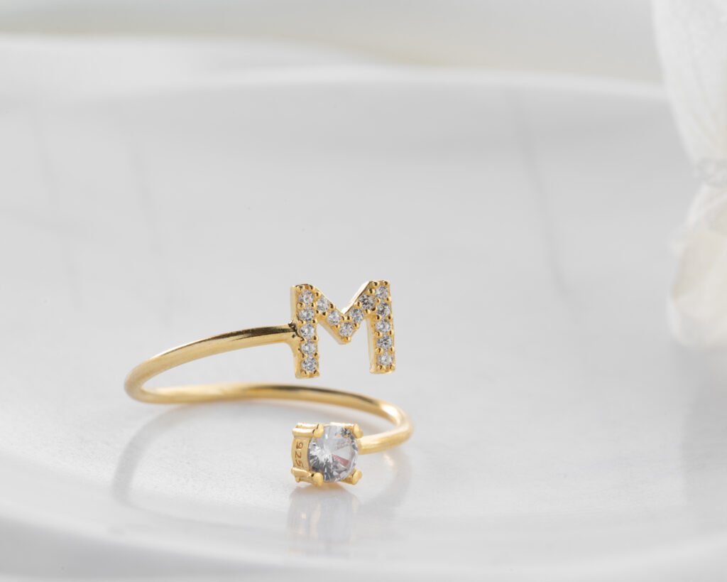 gold initial ring “M” with solitaire stone on light background