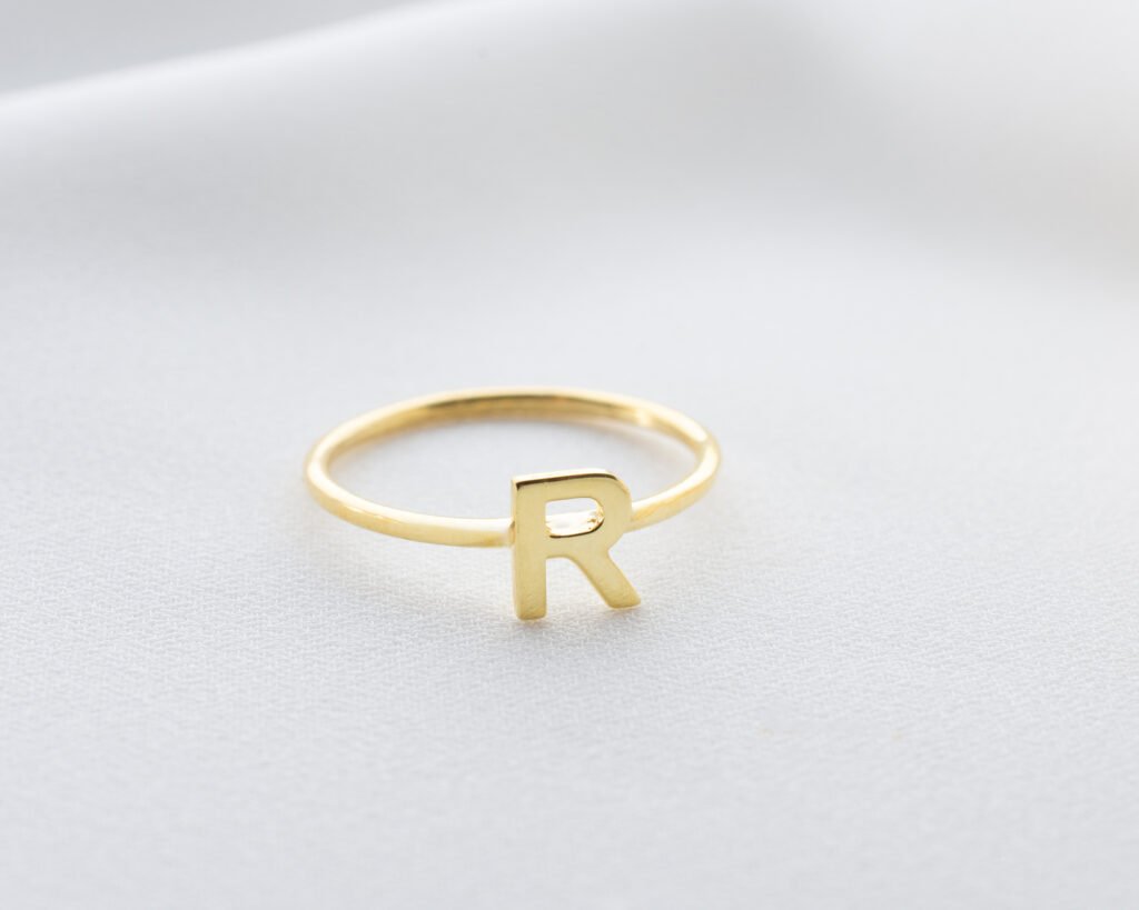 gold-plated “R” initial ring on textured surface