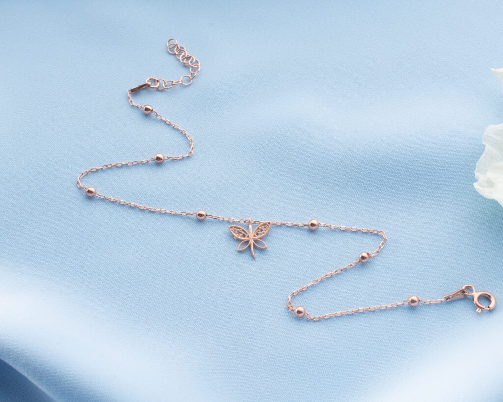 rose gold butterfly anklet displayed on soft blue fabric