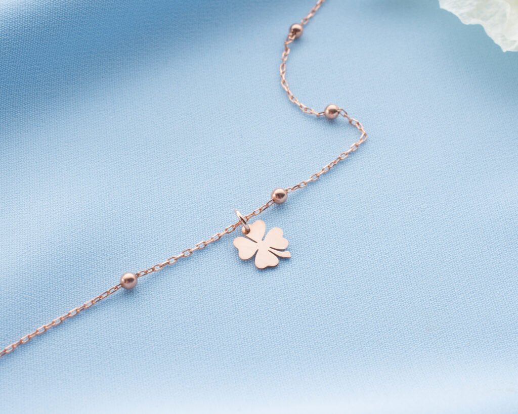 rose gold clover anklet displayed on soft blue fabric
